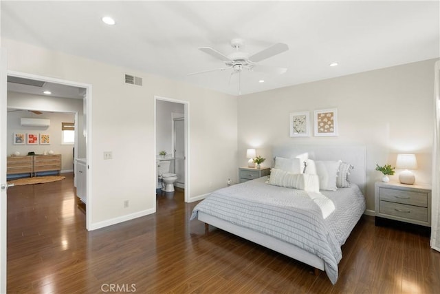 bedroom featuring ceiling fan, ensuite bathroom, dark hardwood / wood-style flooring, and an AC wall unit