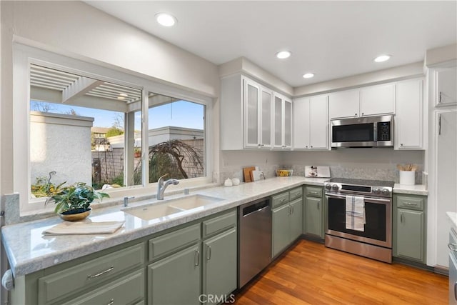 kitchen with white cabinetry, sink, green cabinetry, stainless steel appliances, and light hardwood / wood-style flooring