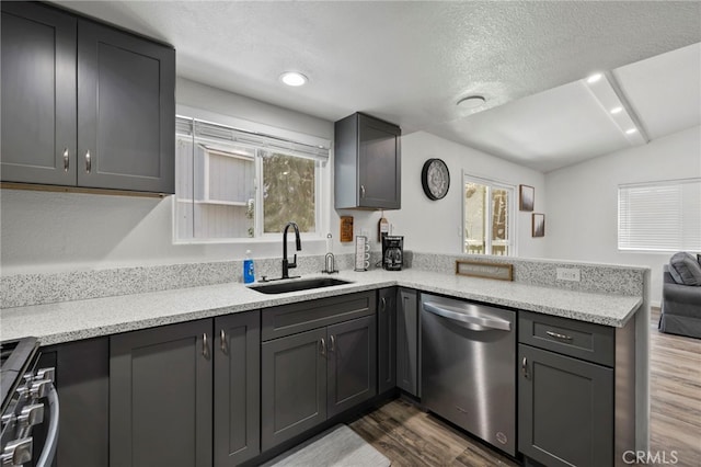 kitchen featuring lofted ceiling, sink, stainless steel appliances, a textured ceiling, and kitchen peninsula