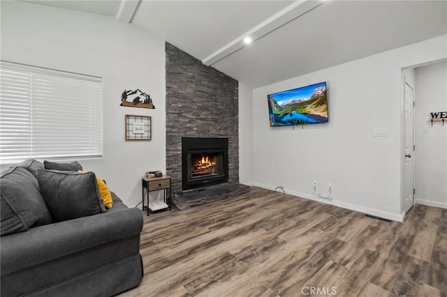 living room with lofted ceiling with beams, a stone fireplace, and hardwood / wood-style floors