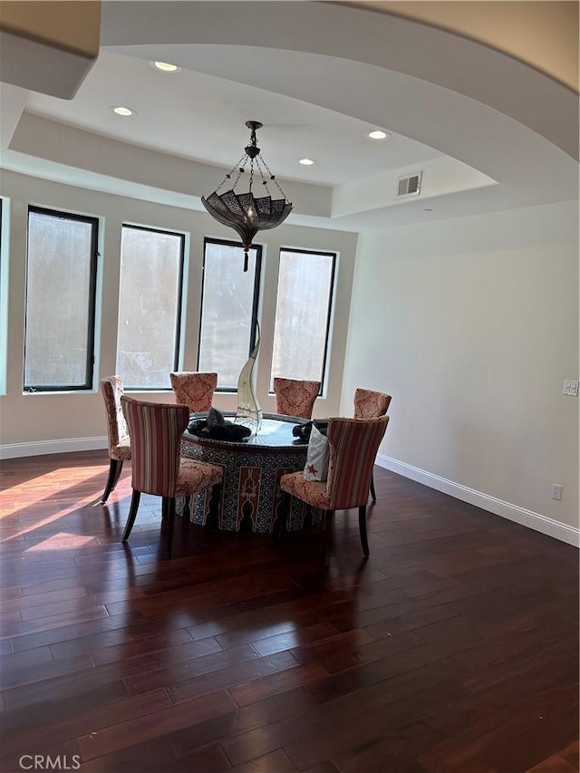 dining room with dark hardwood / wood-style flooring, a raised ceiling, and a notable chandelier