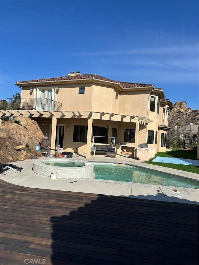 back of property with a swimming pool with hot tub, a patio, and a balcony