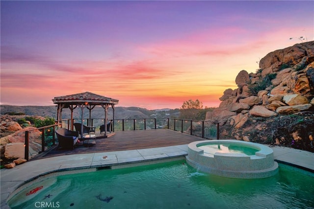 pool at dusk featuring a gazebo, a deck with mountain view, and an in ground hot tub