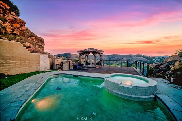 pool at dusk featuring a mountain view, a gazebo, pool water feature, and an in ground hot tub