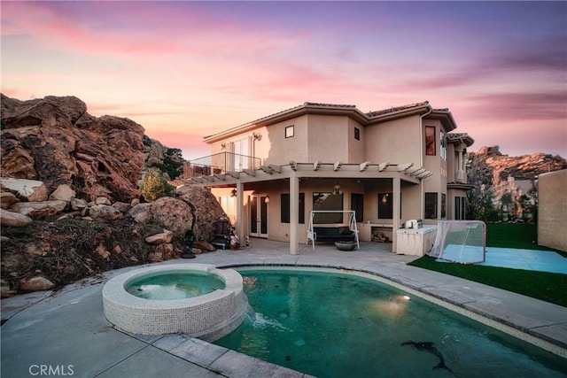 back house at dusk featuring a balcony, a pergola, a pool with hot tub, and a patio area