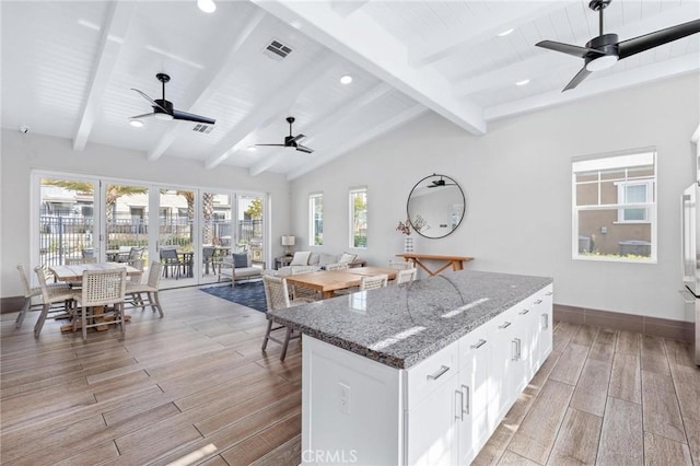 kitchen featuring white cabinetry, a center island, lofted ceiling with beams, dark stone countertops, and ceiling fan