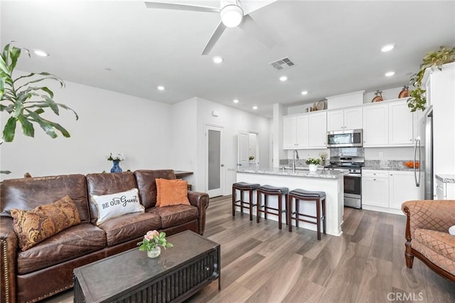 living room with ceiling fan, sink, and light wood-type flooring