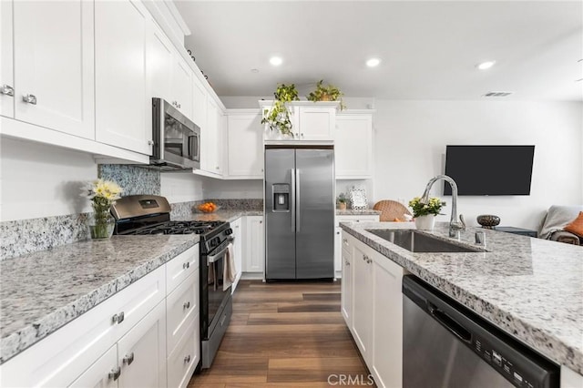 kitchen featuring appliances with stainless steel finishes, dark hardwood / wood-style floors, sink, white cabinets, and light stone countertops