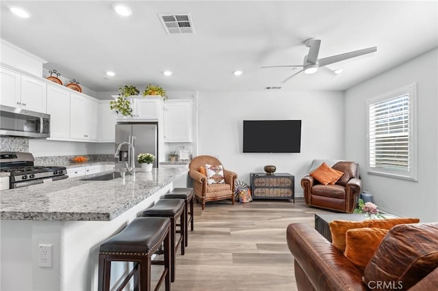 kitchen with sink, light wood-type flooring, appliances with stainless steel finishes, a kitchen breakfast bar, and white cabinets