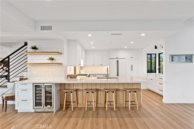 kitchen featuring wine cooler, a breakfast bar, high end fridge, sink, and white cabinetry