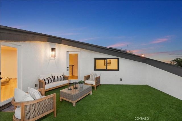 back house at dusk with an outdoor living space and a lawn