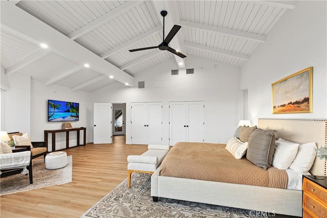 bedroom with two closets, high vaulted ceiling, ceiling fan, beam ceiling, and light hardwood / wood-style flooring