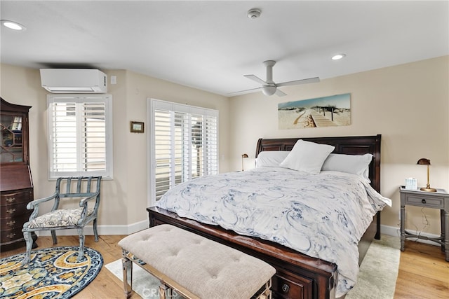 bedroom with multiple windows, a wall unit AC, and light hardwood / wood-style flooring