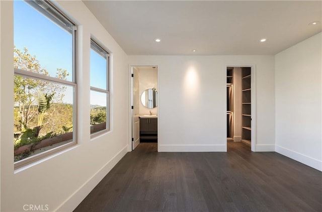 unfurnished bedroom with sink, ensuite bath, dark hardwood / wood-style floors, and a spacious closet