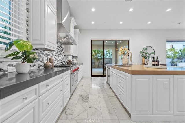 kitchen featuring wall chimney range hood, sink, double oven range, tasteful backsplash, and white cabinets