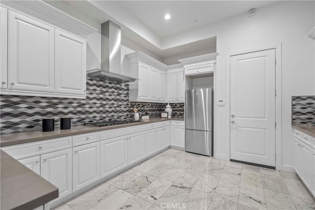 kitchen with tasteful backsplash, white cabinets, appliances with stainless steel finishes, and wall chimney range hood