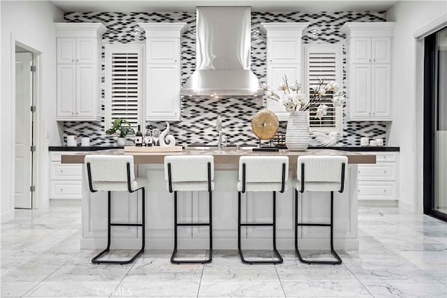 kitchen featuring white cabinets, a kitchen breakfast bar, and wall chimney exhaust hood