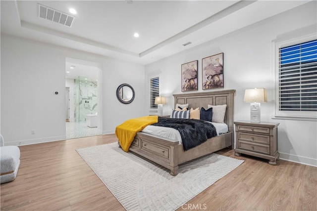 bedroom with connected bathroom, light hardwood / wood-style floors, and a raised ceiling