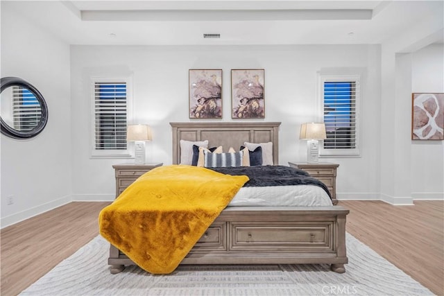 bedroom with a tray ceiling and light wood-type flooring