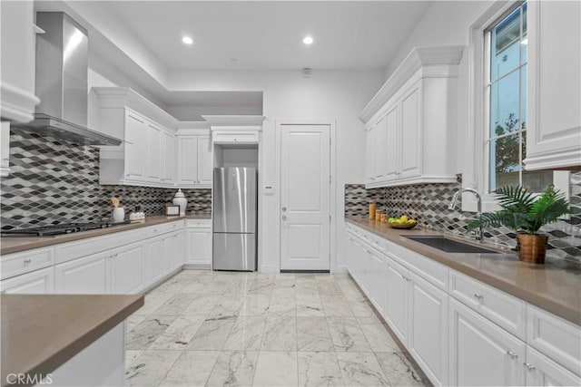 kitchen featuring tasteful backsplash, sink, white cabinets, stainless steel appliances, and wall chimney exhaust hood