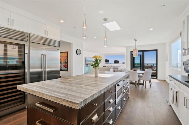 kitchen featuring dark brown cabinetry, white cabinetry, decorative light fixtures, dark hardwood / wood-style flooring, and a kitchen island