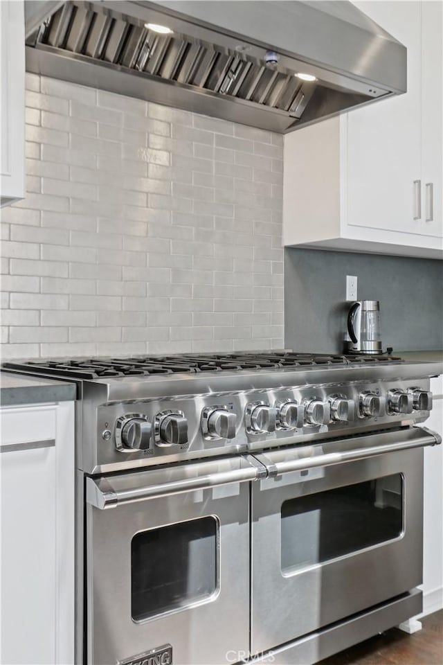 kitchen with backsplash, white cabinets, wall chimney range hood, and range with two ovens