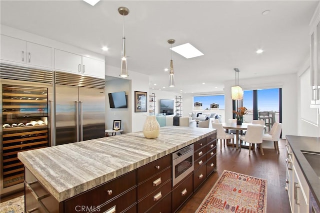 kitchen with dark wood-style floors, beverage cooler, dark brown cabinets, built in appliances, and white cabinetry