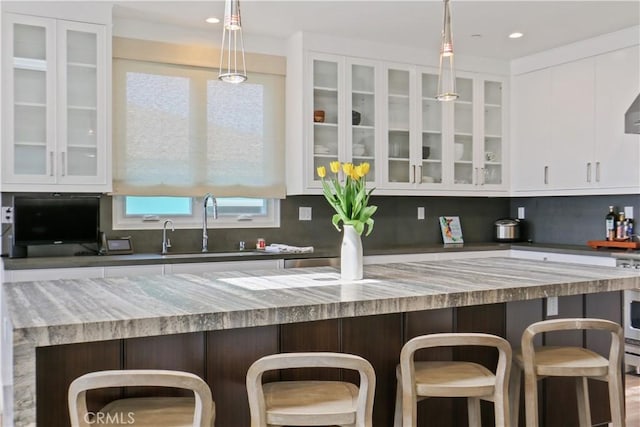 kitchen featuring a sink, glass insert cabinets, tasteful backsplash, and white cabinets