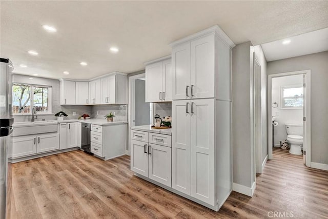 kitchen with white cabinetry, sink, backsplash, and light hardwood / wood-style flooring