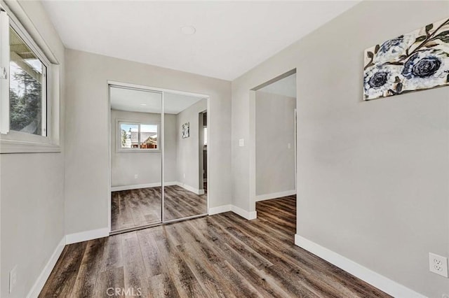 unfurnished bedroom featuring multiple windows, dark wood-type flooring, and a closet