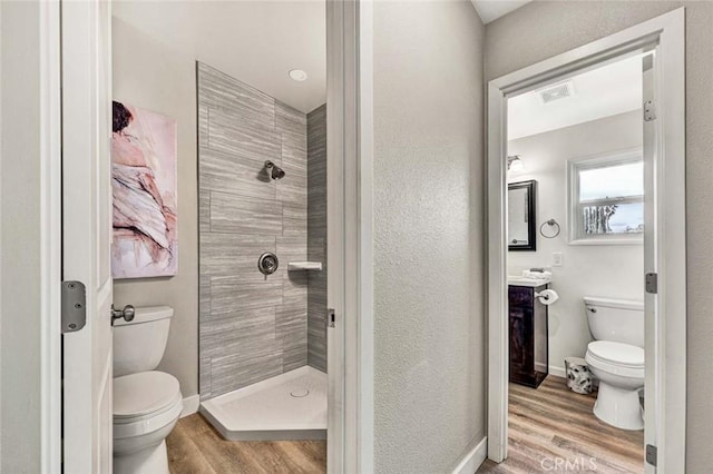 bathroom featuring vanity, hardwood / wood-style flooring, toilet, and tiled shower