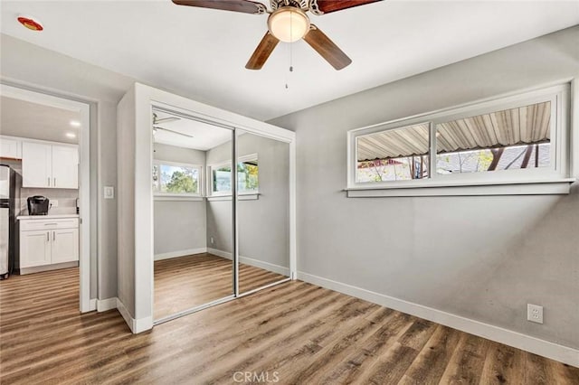 unfurnished bedroom featuring ceiling fan, wood-type flooring, stainless steel fridge, and a closet