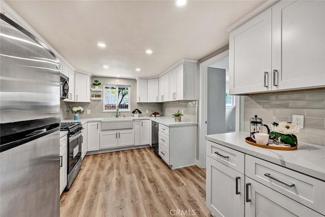 kitchen with appliances with stainless steel finishes, sink, white cabinets, backsplash, and light stone countertops