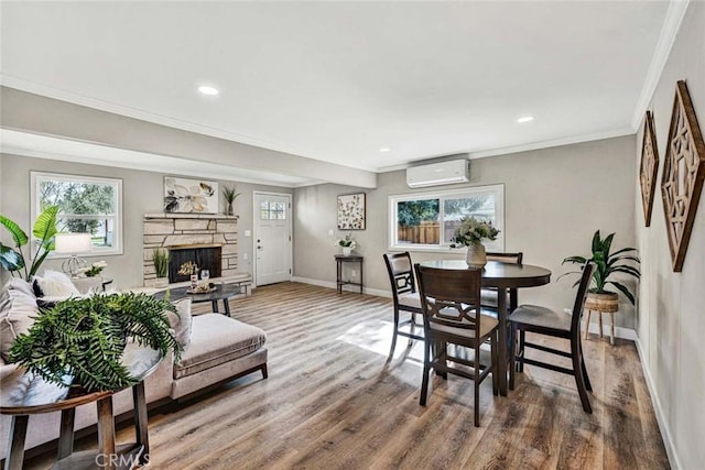 dining space featuring a fireplace, hardwood / wood-style floors, a wall unit AC, and a wealth of natural light