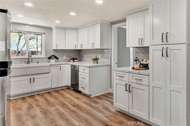 kitchen with appliances with stainless steel finishes, sink, white cabinets, decorative backsplash, and light hardwood / wood-style floors