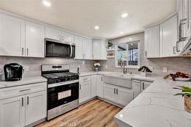 kitchen with light stone countertops, white cabinetry, appliances with stainless steel finishes, and light hardwood / wood-style floors