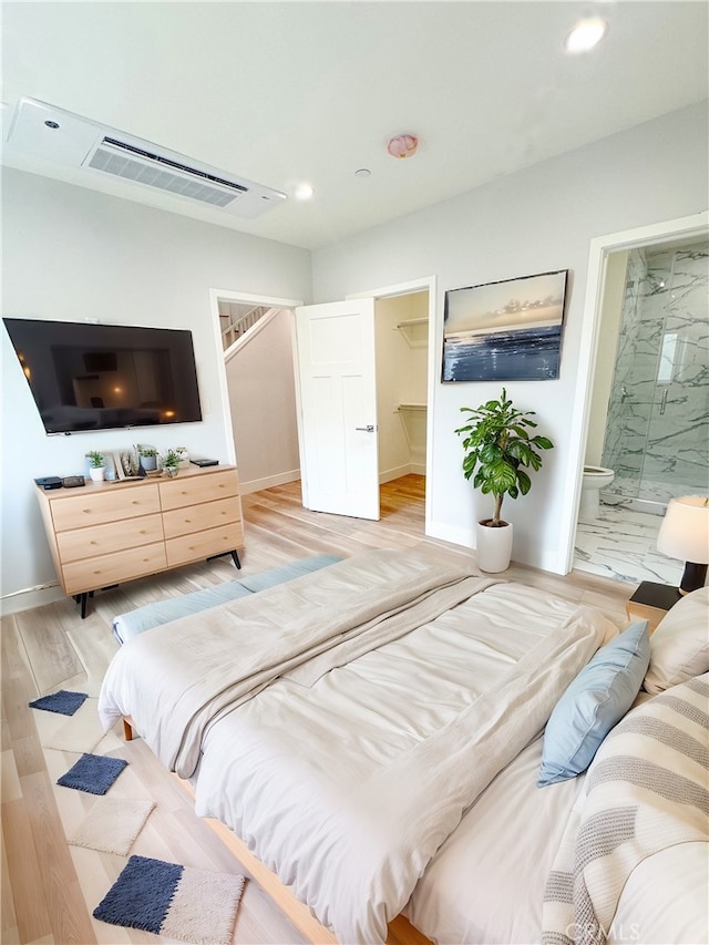 bedroom with a spacious closet, ensuite bath, and light hardwood / wood-style floors