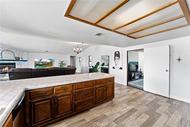 kitchen featuring dark brown cabinets, tile countertops, a fireplace, and light hardwood / wood-style flooring