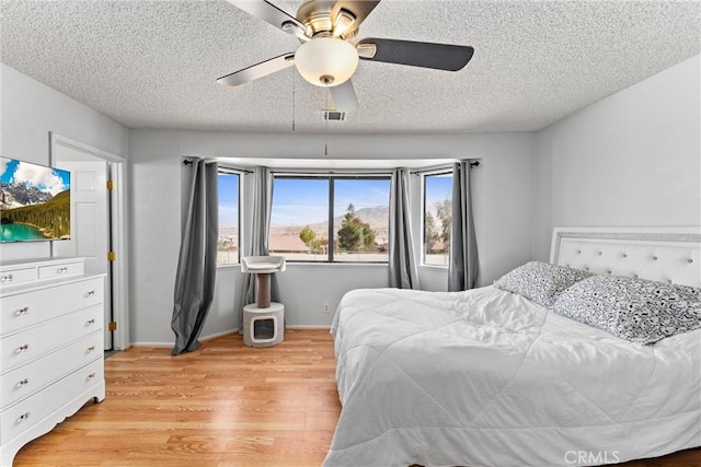 bedroom featuring ceiling fan, light hardwood / wood-style floors, and a textured ceiling