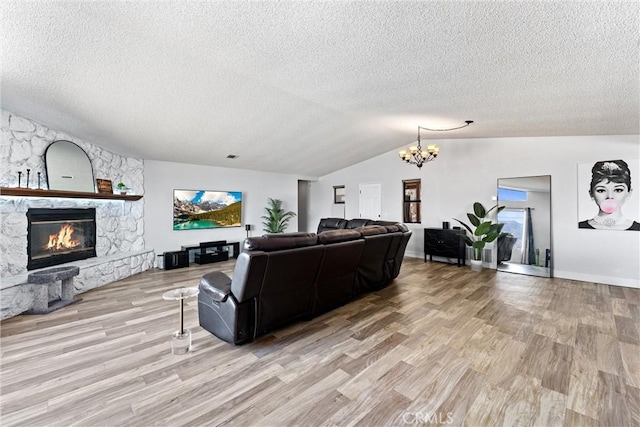 living room with an inviting chandelier, a stone fireplace, vaulted ceiling, and light hardwood / wood-style floors