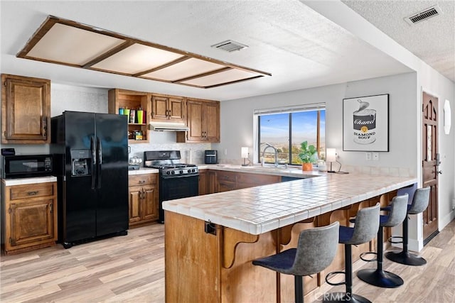 kitchen with tile countertops, kitchen peninsula, a kitchen breakfast bar, and black appliances