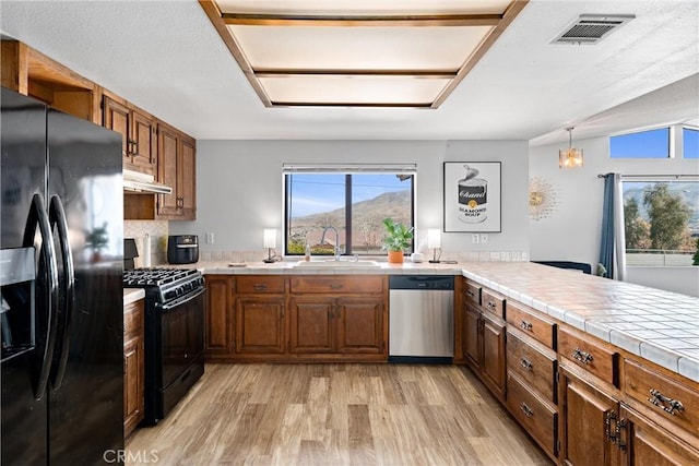 kitchen with sink, decorative light fixtures, tile counters, a mountain view, and black appliances