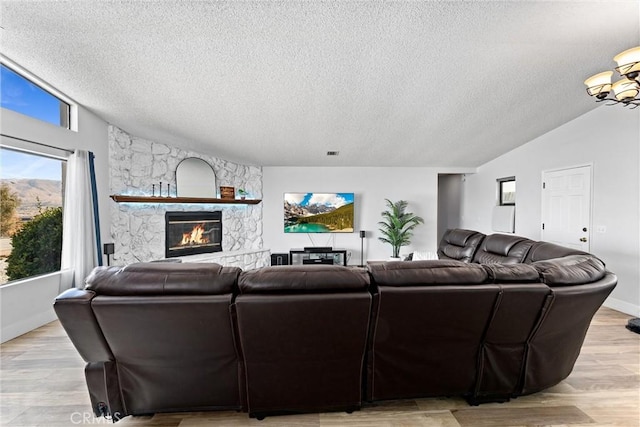 living room featuring a stone fireplace, vaulted ceiling, light hardwood / wood-style flooring, and a textured ceiling