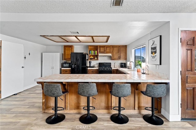 kitchen with sink, a breakfast bar, tile counters, black appliances, and kitchen peninsula