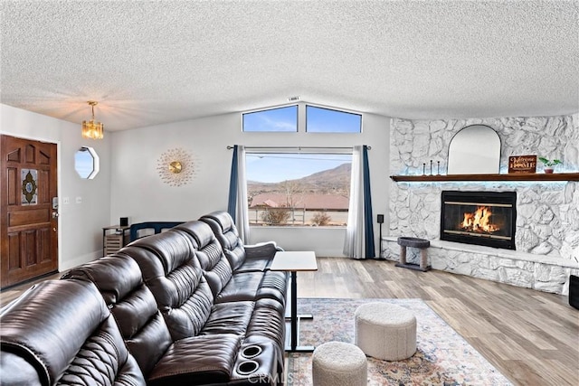 living room with a stone fireplace, lofted ceiling, a mountain view, a textured ceiling, and light hardwood / wood-style flooring