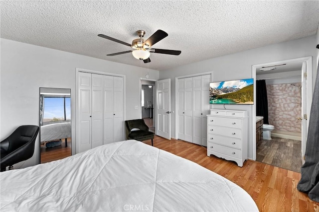 bedroom featuring ensuite bath, hardwood / wood-style flooring, ceiling fan, multiple closets, and a textured ceiling