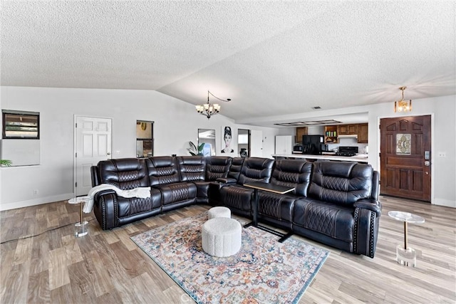 living room with an inviting chandelier, vaulted ceiling, a textured ceiling, and light wood-type flooring