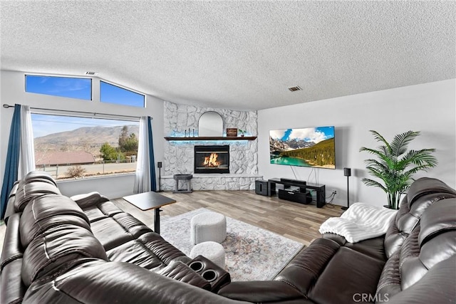 living room with vaulted ceiling, a stone fireplace, a textured ceiling, and a mountain view