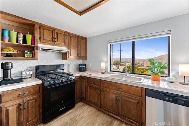 kitchen featuring sink, stainless steel dishwasher, tile counters, and black gas range oven