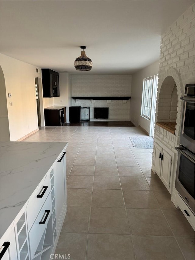 kitchen with white cabinetry, light tile patterned floors, double oven, brick wall, and light stone countertops